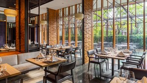 Een restaurant met hoge plafonds, grote ramen en een modern interieur. Tafels zijn gedekt met witte servetten en glazen.