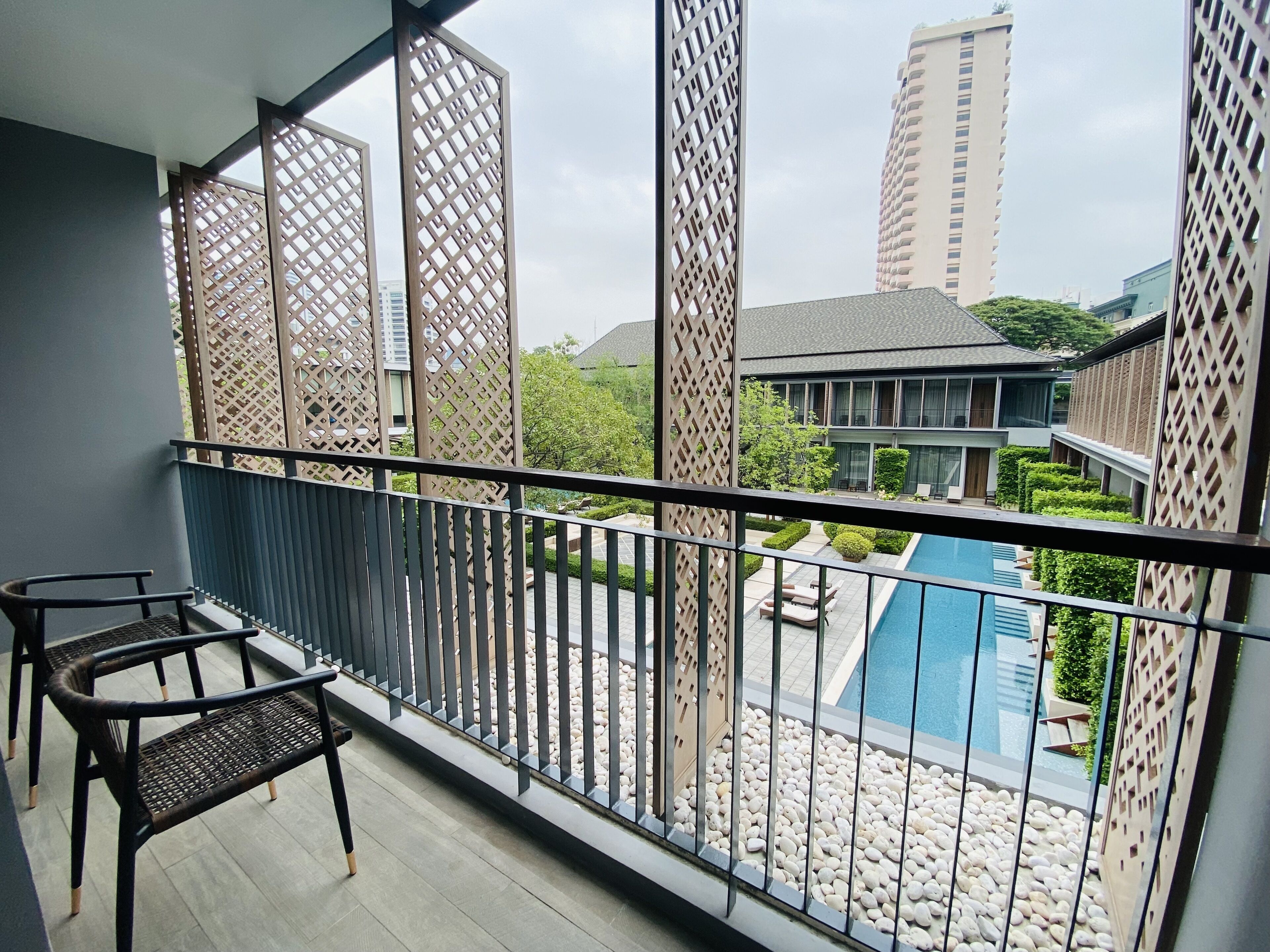 A balcony with a view of a swimming pool, a building with a modern design, and a clear sky.