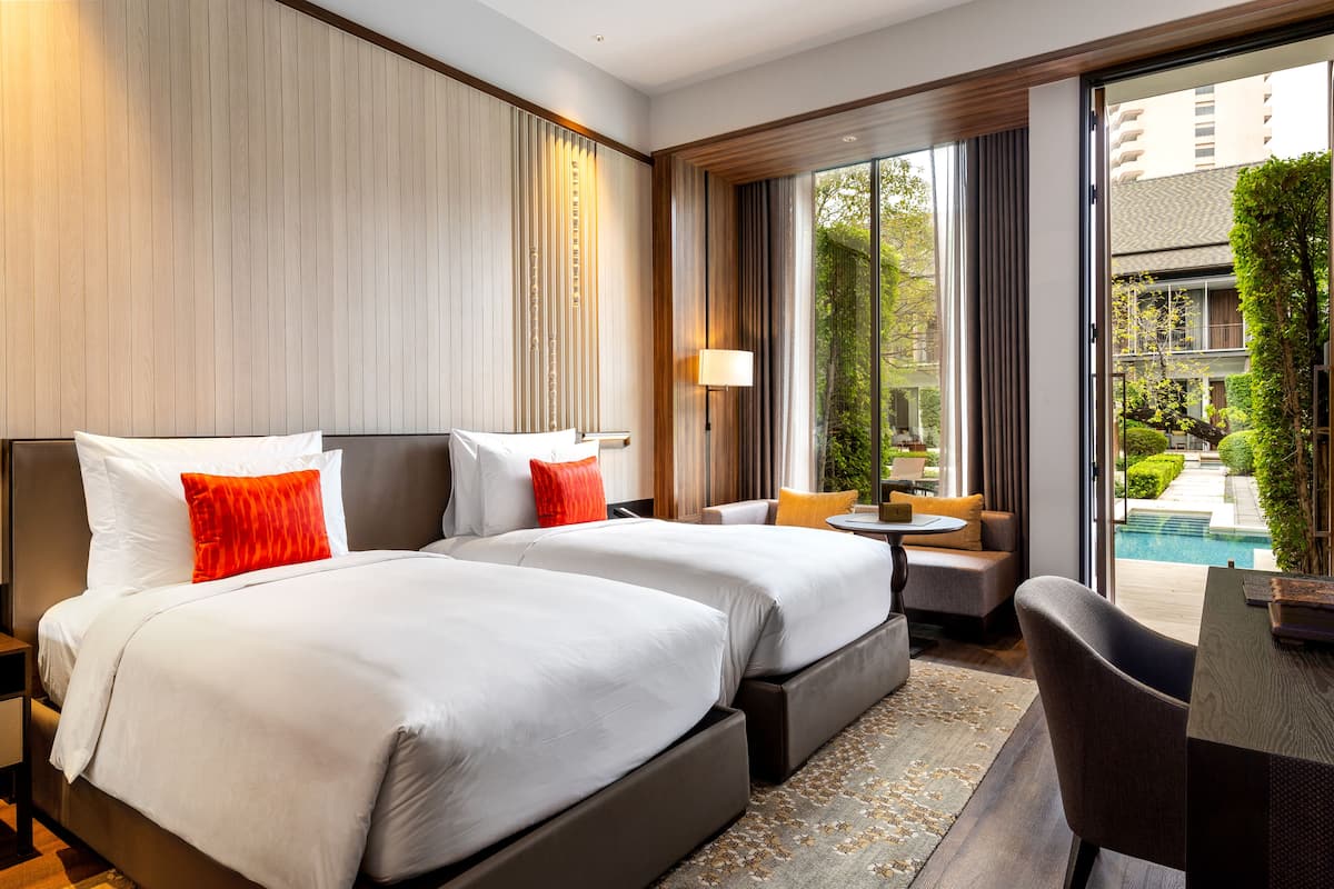 A hotel room with two beds, a desk, and a view of a swimming pool.