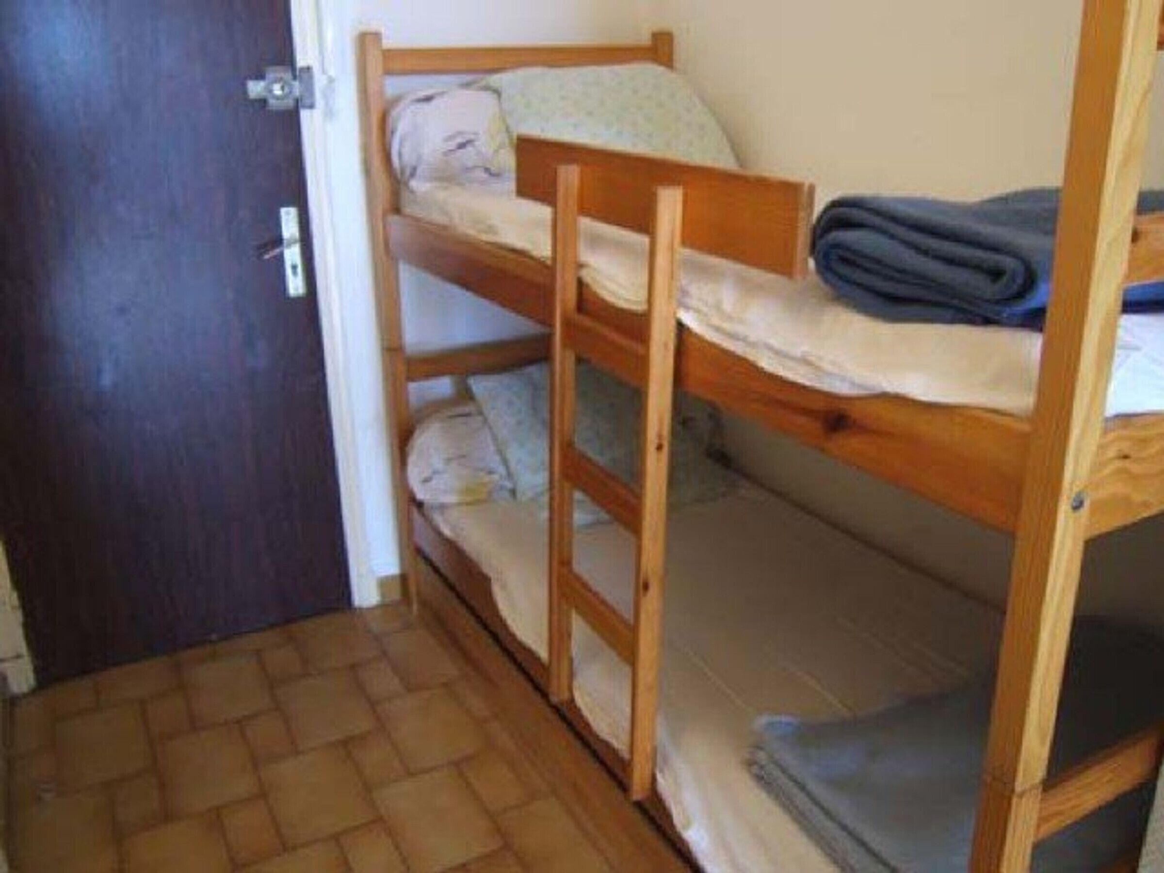 Une chambre avec un lit superposé, une porte en bois et un sol carrelé.