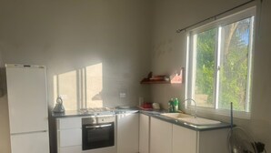 Cozinha equipada com frigorífico, fogão, forno, pia e janela com vista para o verde.