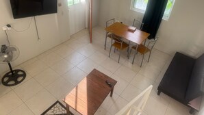 Quarto com televisão na parede, mesa de jantar com cadeiras, ventoinha e janela com cortinas.