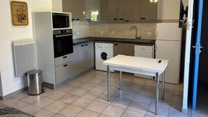 A compact kitchen with a washing machine, oven, microwave, and a small table.