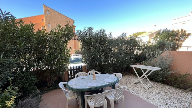 An outdoor patio with a round table and chairs, surrounded by greenery and a gravel path.