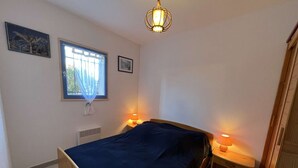 A bedroom with a wooden bed, two bedside tables with lamps, a window with a curtain, and a radiator.