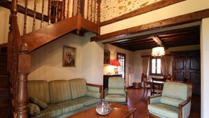 A cozy living room with a wooden staircase, a green sofa, two armchairs, a wooden coffee table, and a dining area with a table and chairs. - Country house in the heart of the bearn180 m2 (Sault-de-Navailles)
