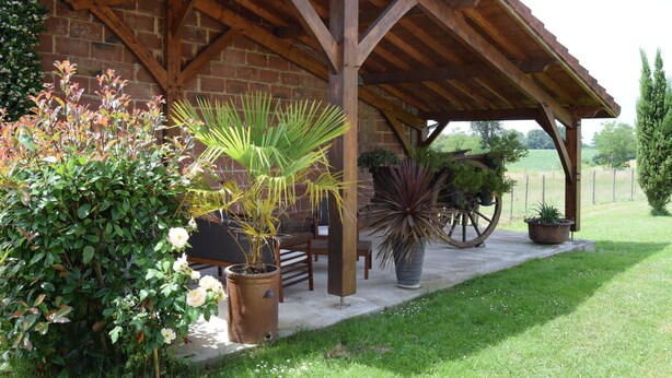 A covered patio with a brick wall, wooden beams, and potted plants. - Country house in the heart of the bearn180 m2 (Sault-de-Navailles)