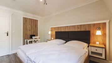 A bedroom with a large bed, two bedside tables with lamps, a wooden headboard, and a desk with a chair.