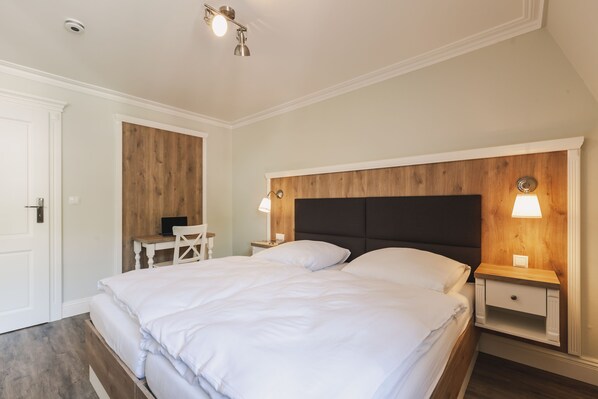 A bedroom with a large bed, two bedside tables with lamps, a wooden headboard, and a desk with a chair.