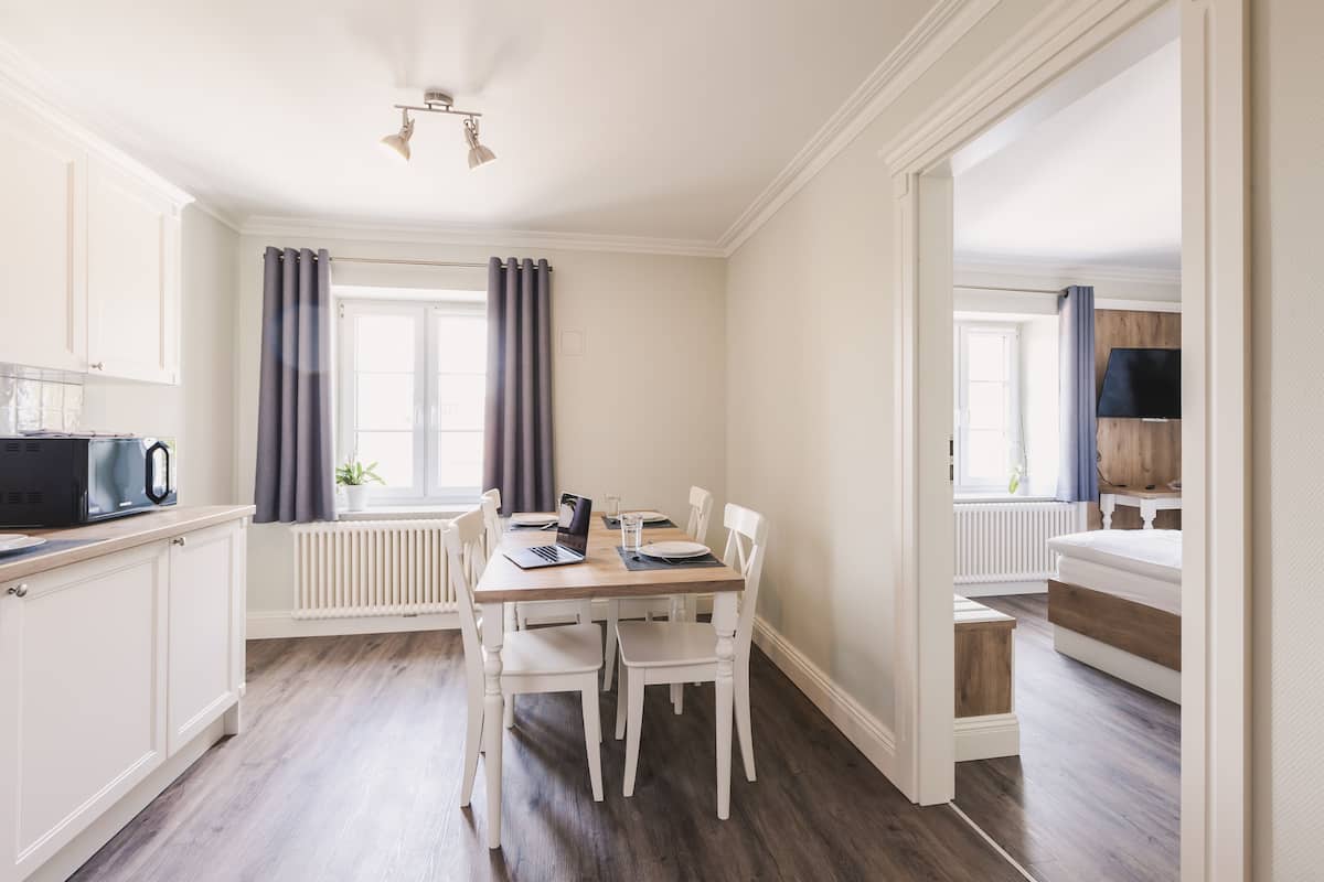 Een moderne keuken met witte kastjes, een eettafel met stoelen, een magnetron en een laptop.