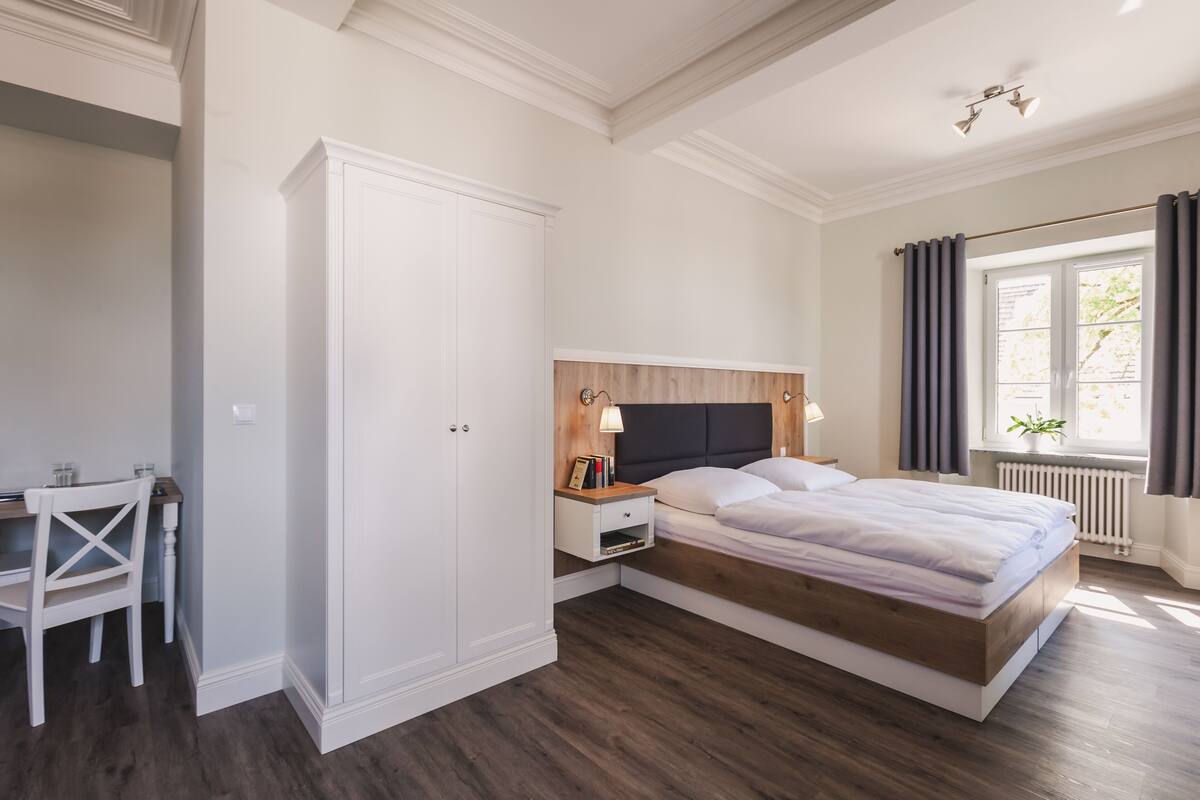 Een slaapkamer met een bed, nachtkastje, kledingkast en bureau met stoel.