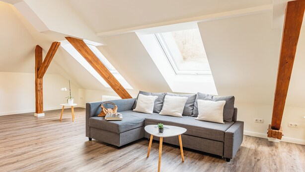 Una habitación moderna estilo loft con un sofá seccional gris, una mesita redonda y vigas de madera.