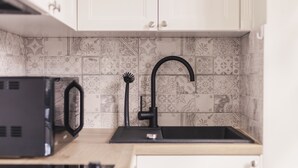 Una cocina con baldosas estampadas, un grifo negro y un microondas.
