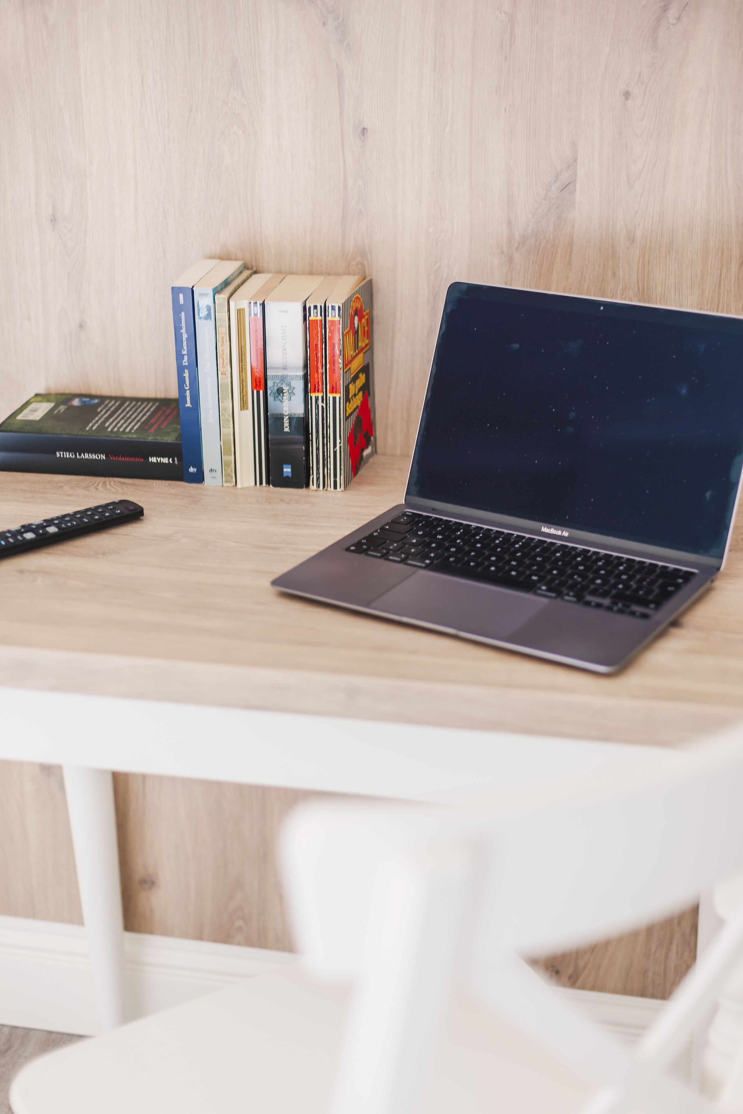 A laptop on a wooden desk with books and a remote control.