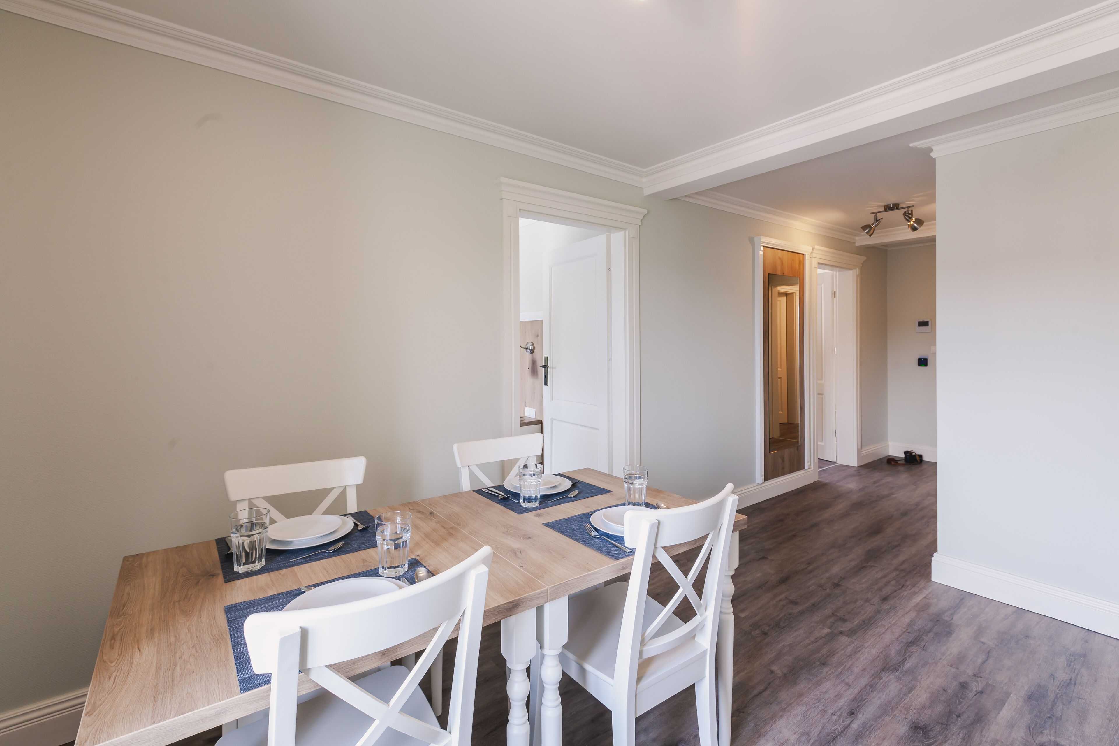 A dining area with a wooden table, white chairs, and a light-colored floor.