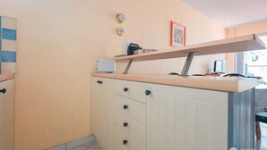A kitchen with a white countertop, a toaster, a coffee maker, and a framed picture on the wall. - Cozy Apartment Near Beach and Shops, with Balcony and Modern Amenities (Les Sables-d'Olonne)
