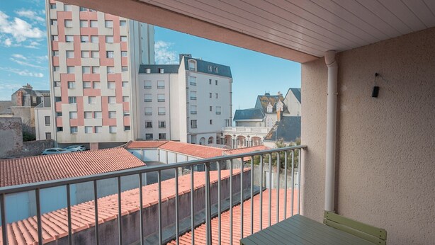 A balcony with a view of a cityscape, including buildings with red-tiled roofs and a tall pink and white building. - Cozy Apartment Near Beach and Shops, with Balcony and Modern Amenities (Les Sables-d'Olonne)