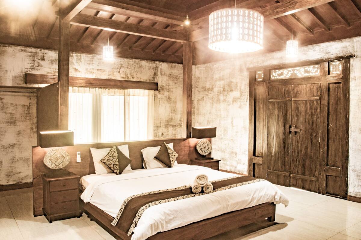 Une chambre à coucher avec un grand lit, une tête de lit en bois, des lampes de chevet et une armoire en bois.