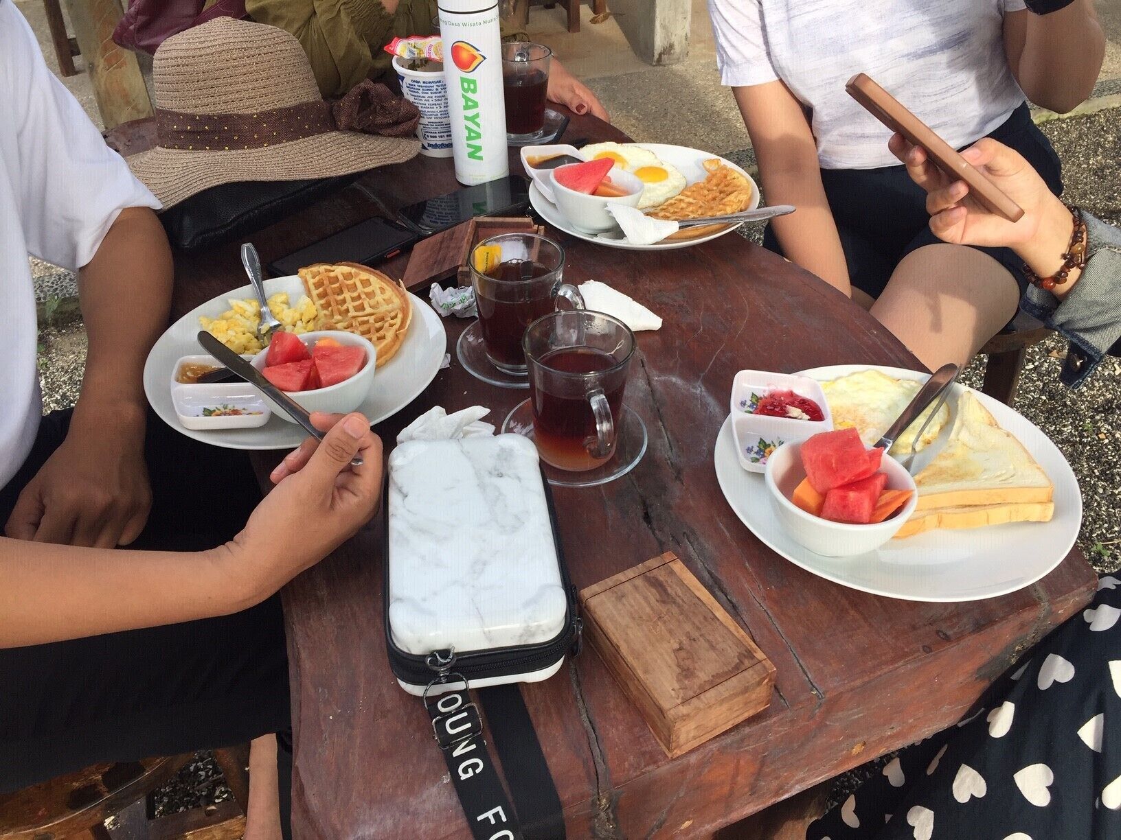 A wooden table with plates of food, a bottle of Bayan, and a small container.