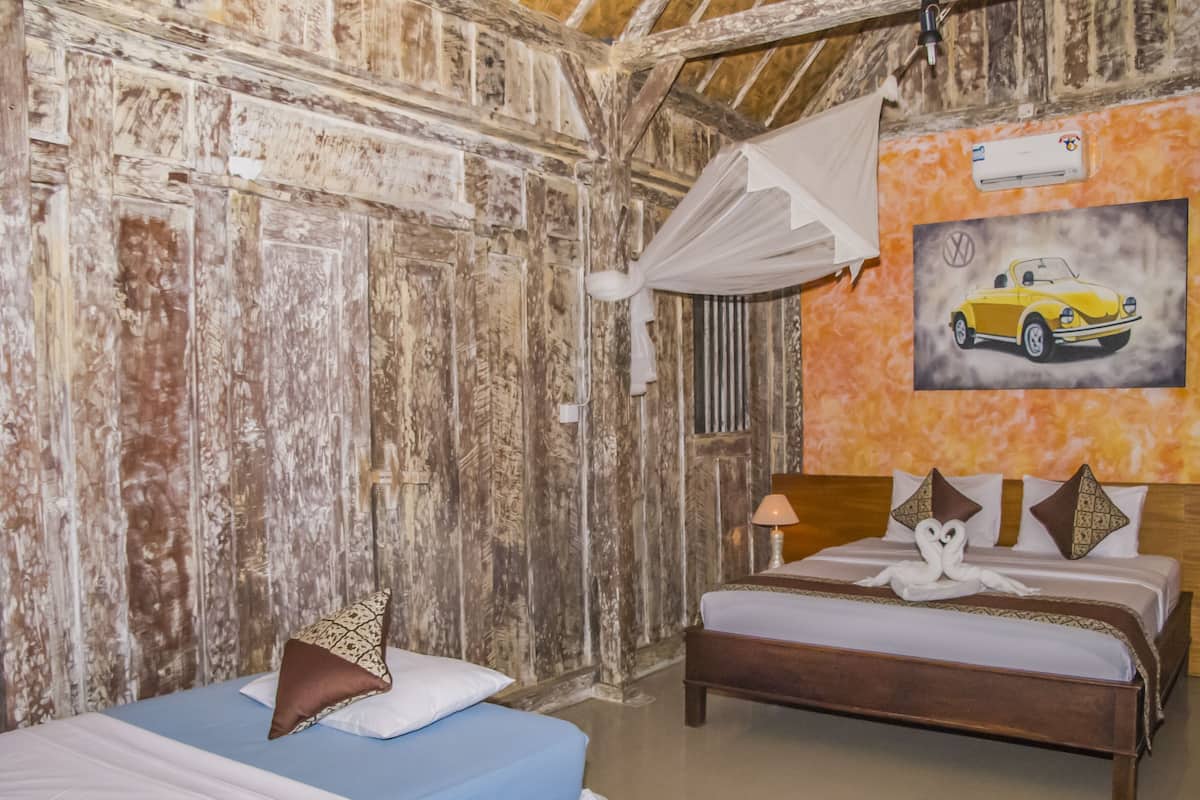 Une pièce aux murs recouverts de bois rustique, un lit avec une literie blanche et bleue, une table de chevet avec une lampe, et un tableau représentant une voiture accroché au mur.