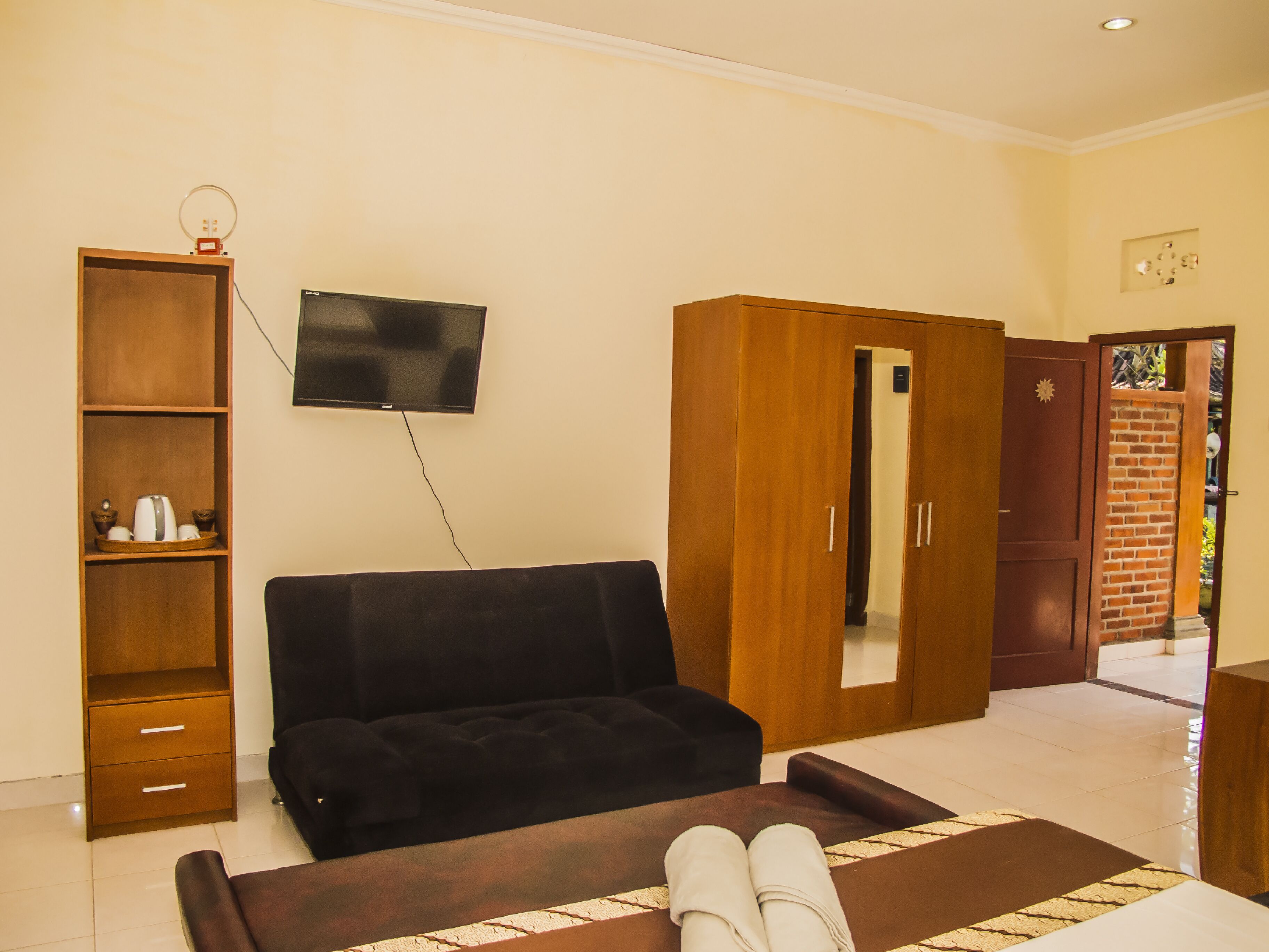 A living room with a black sofa, a wooden cabinet, a television mounted on the wall, and a wooden wardrobe with a mirror.