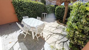 An outdoor patio with a table and chairs, surrounded by greenery and a building in the background. - 2-room apartment with pool, 4 ppl, Cap d'Agde (Cap d'Agde)
