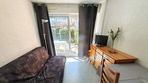 A small, modern room with a sofa, a bed, a wooden desk, and a television. - 2-room apartment with pool, 4 ppl, Cap d'Agde (Cap d'Agde)