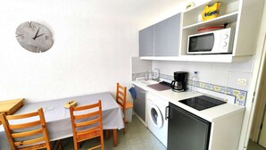 A compact kitchen with a dining table, chairs, a washing machine, a microwave, and a coffee maker. - 2-room apartment with pool, 4 ppl, Cap d'Agde (Cap d'Agde)