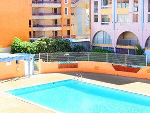 A swimming pool with a metal fence, surrounded by multi-story buildings with balconies. - 2-room apartment with pool, 4 ppl, Cap d'Agde (Cap d'Agde)
