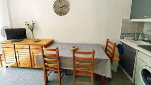A compact kitchen with a dining area, a washing machine, and a clock on the wall. - 2-room apartment with pool, 4 ppl, Cap d'Agde (Cap d'Agde)