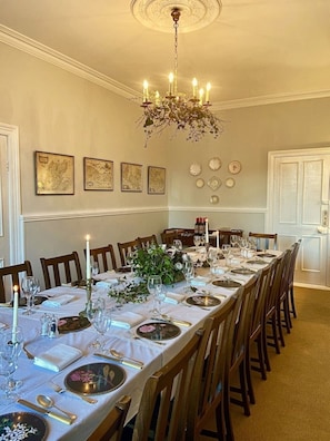 Un comedor formal con una larga mesa dispuesta para una comida, rodeada de sillas de madera.