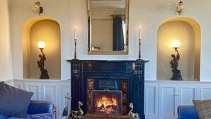A room with a fireplace, two sofas, a wooden chest, and wall sconces. - Clifden's premier holiday home with heated pool + sauna - sleeps 24 (Clifden)