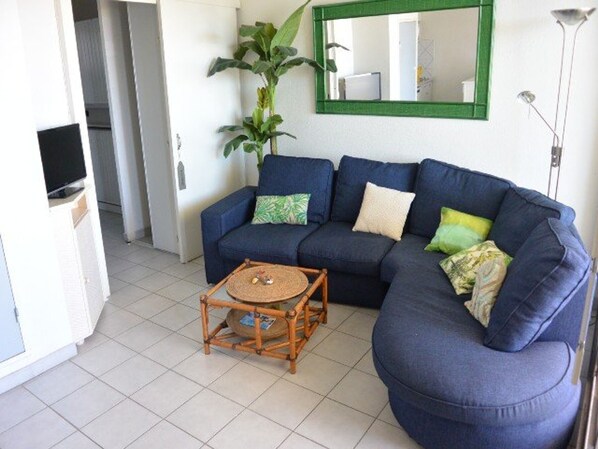 A living room with a blue sofa, a small wooden coffee table, and a green plant. - Charming T2 with Terrace and Sea View 50m from Beach, Residence with Pool (Cap d'Agde)