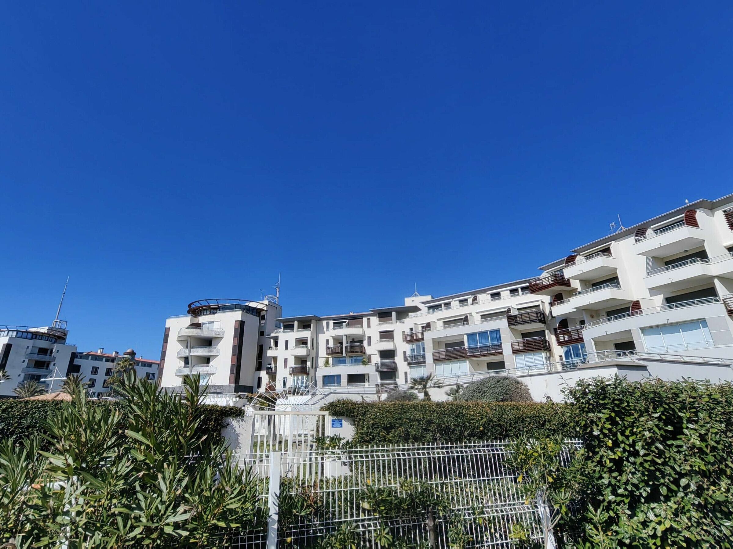A multi-story residential building with balconies, a gated entrance, and a clear blue sky.