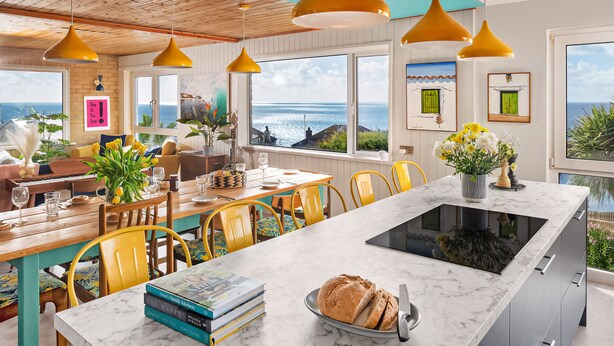 A modern kitchen with a marble countertop, yellow chairs, and a view of the sea. - Sunset Beach House, Porthleven, with panoramic sea views. Comfortably sleeps 10 (Porthleven)