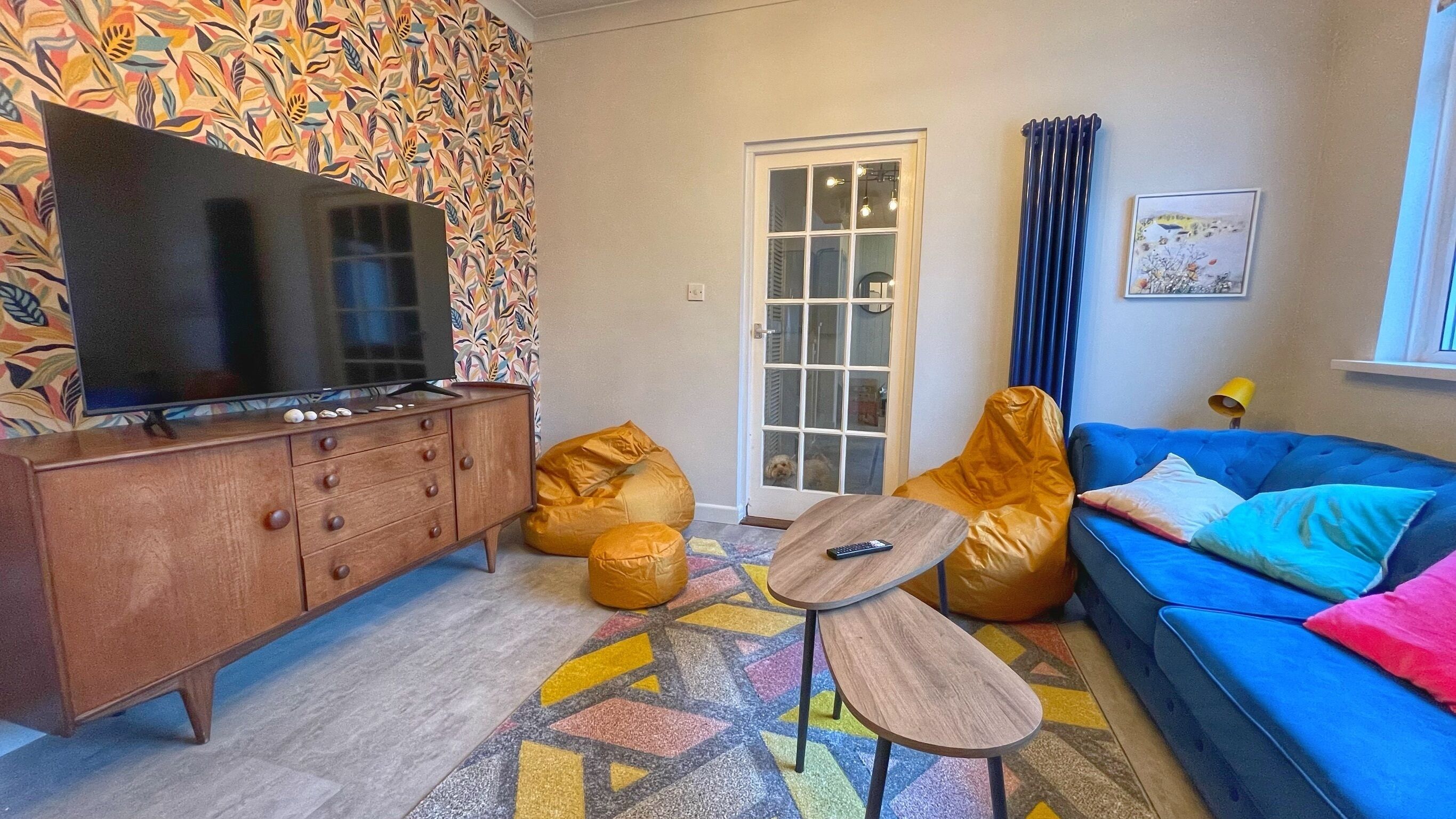 A living room with a TV, wooden cabinet, colorful rug, and a blue sofa.