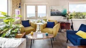 A cozy room with yellow and blue sofas, a wooden coffee table, and a view of the sea through large windows. - Sunset Beach House, Porthleven, with panoramic sea views. Comfortably sleeps 10 (Porthleven)