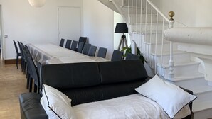 A spacious room with a black sofa, white cushions, a dining table with chairs, and a white staircase. - A charming Domaine de La Béchetière, located 2h15 from Paris! (Parcé-sur-Sarthe)