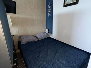 Una habitación pequeña con una cama individual, cabecera de madera, mesita de noche con lámpara y una composición de fotos en la pared.