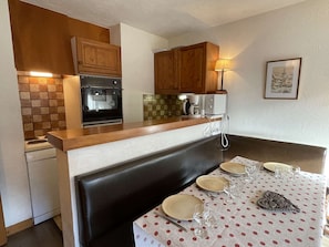 A compact kitchen with wooden cabinets, a built-in oven, a coffee maker, and a dining area with a table set for four.