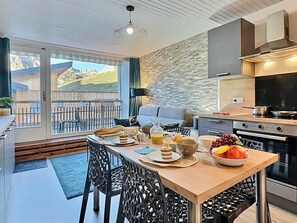 Uma cozinha moderna com área de refeições, uma janela grande com vista para montanhas e uma varanda com mobiliário de exterior.