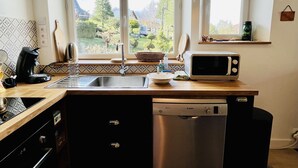 Een compacte keuken met een vaatwasser, een magnetron en een spoelbak. Twee ramen bieden uitzicht op een bergachtig landschap.