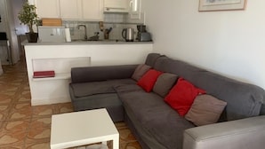 A living room with a grey sofa, a white coffee table, and a kitchen area in the background. - Bright T2 with Balcony near the Thermal Baths (Balaruc-les-Bains)