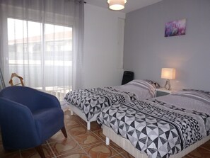 A bedroom with two beds, a chair, a desk, and a lamp.