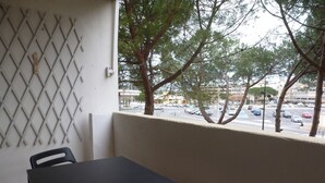 A balcony with a table and chairs, overlooking a street with cars and trees. - Bright T2 with Balcony near the Thermal Baths (Balaruc-les-Bains)