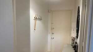 A hallway with a white door, a coat rack, a small table with a chair, and a tiled floor. - Bright T2 with Balcony near the Thermal Baths (Balaruc-les-Bains)