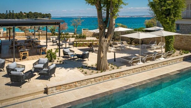 A poolside area with lounge chairs and umbrellas, a covered seating area, and a view of the sea. - DUNATOVI DVORI Heritage Hotel (Preko)