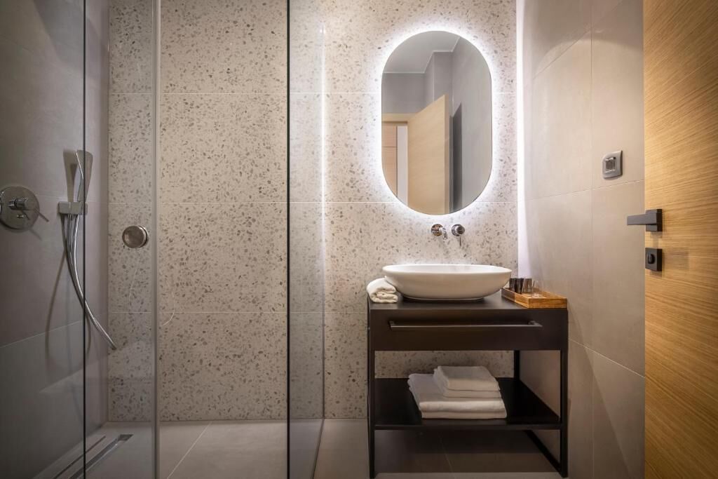 Une salle de bain moderne avec une douche à l’italienne, un miroir rond et un meuble-lavabo en bois foncé.