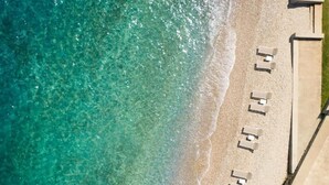 An aerial view of a beach with clear turquoise water and a row of sun loungers aligned along the shoreline. - DUNATOVI DVORI Heritage Hotel (Preko)