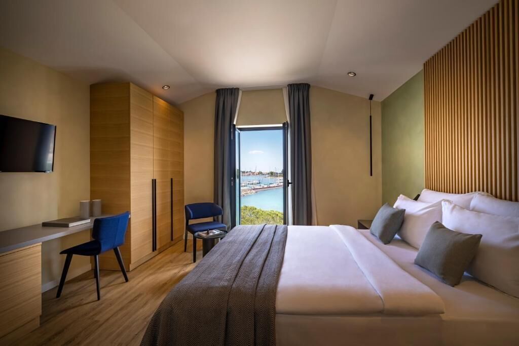 A modern hotel room with a large bed, a desk, a chair, and a TV.